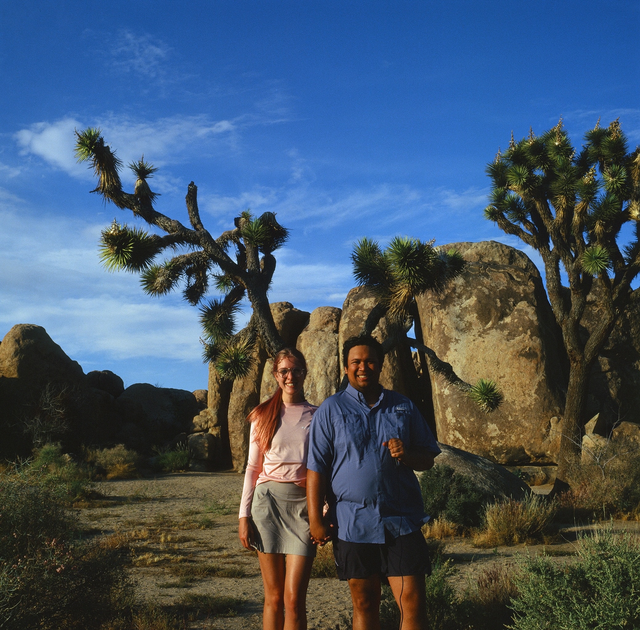 Nathaniel and his wife Kelsie holding hands with a desert scene and a Joshua tree in the background